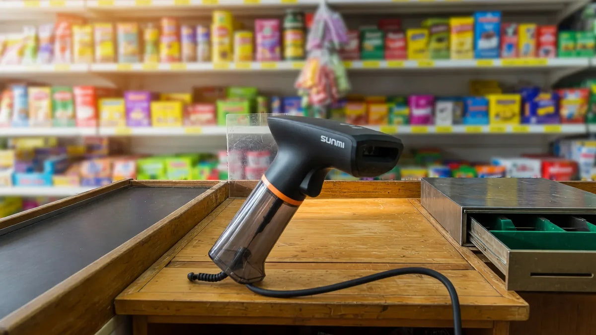 Douchette code-barres Sunmi filaire posée sur le comptoir en bois d'une épicerie